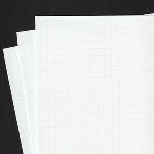 Könnte beinhalten: Nahaufnahme von drei weißen, karierten Papierblättern. Das Papier hat eine strukturierte Oberfläche und ein dezentes Rastermuster, ideal zum Schreiben oder Zeichnen. Die Blätter sind vor einem dunklen Hintergrund gestapelt.