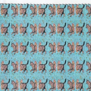 May include: A sheet of perforated squares featuring a repeating pattern of brown tabby cats stepping through colorful portals on a light blue background. Small gold stars are scattered throughout the design.