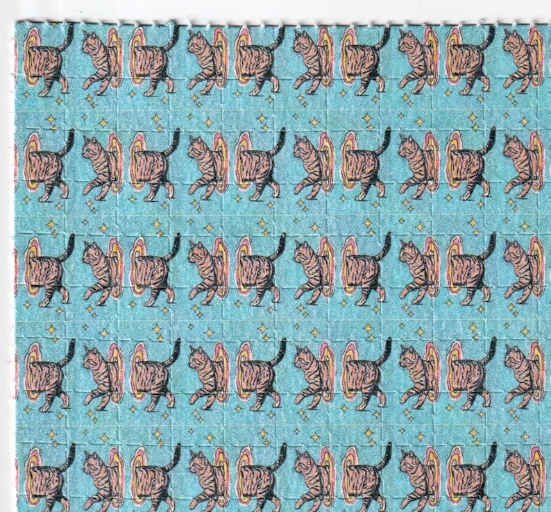 May include: A sheet of perforated squares featuring a repeating pattern of brown tabby cats stepping through colorful portals on a light blue background. Small gold stars are scattered throughout the design.