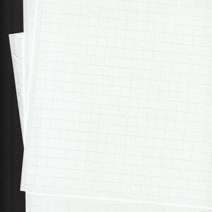 May include: A stack of white, textured paper sheets with a grid pattern. The paper has a subtle, embossed texture and is stacked against a dark background, creating a contrast. The sheets are clean and crisp.