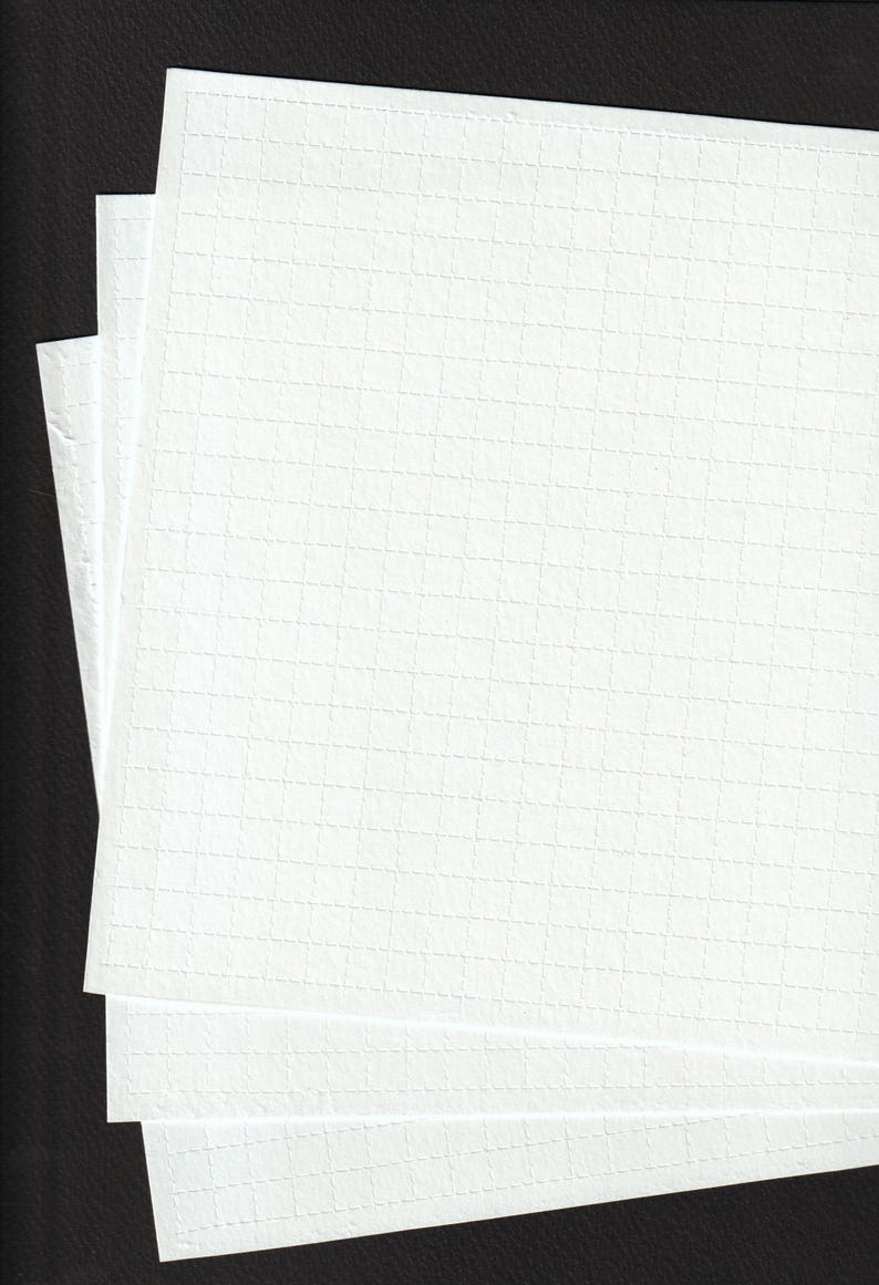 May include: A stack of white, textured paper sheets with a grid pattern. The paper has a subtle, embossed texture and is stacked against a dark background, creating a contrast. The sheets are clean and crisp.