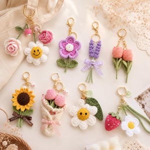 Può includere: Una collezione di portachiavi a fiori all'uncinetto fatti a mano in vari design. Include un girasole, una margherita, una rosa, un tulipano, lavanda e una fragola. Ogni portachiavi ha una chiusura color oro.