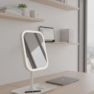 May include: A white, rectangular vanity mirror with an LED border, on a matching base with a pen and sticky note. A laptop and a closed notebook sit on a light wood desk. Shelves and a window are in the background.