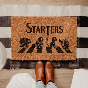 A top-down view of a rectangular natural coir doormat displaying four iconic retro anime characters walking across a street crossing with a person standing on it