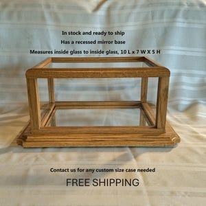 May include: A rectangular wooden display case with a mirrored base and glass sides. The case measures 10 inches long, 7 inches wide, and 5 inches high. The display case is made of light brown wood.