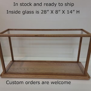 May include: A rectangular display case with a wooden frame and a glass top and sides. The inside glass dimensions are 28" x 8" x 14" high. The base and frame are made of light-colored wood. The text "Custom orders are welcome" is visible.