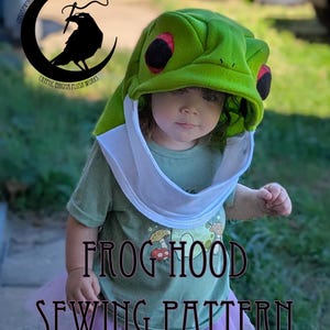 May include: A child wearing a green frog hood with red and black details and a white bib. The text "FROG HOOD SEWING PATTERN" is displayed in a dark brown font. The child is wearing a green t-shirt and a pink tutu.