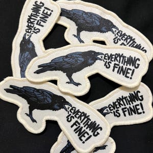 May include: A collection of embroidered patches featuring a black raven with the text "EVERYTHING IS FINE!" in white. The raven is depicted with its beak open, and the patches have a white border.