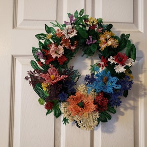 May include: A beaded wreath with a variety of colorful flowers, including red, pink, blue, yellow, and green. The wreath is made of beads and wire and is perfect for decorating a door or wall.