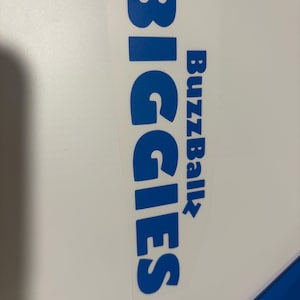 May include: A rectangular adhesive decal featuring the word BIGGIES in large, bold, blue capital letters oriented vertically, with the word BuzzBallz printed in smaller blue letters to the right, all set against a clear, transparent backing.
