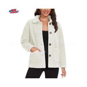 Peut inclure: Veste crème à boutons avec un extérieur texturé et duveteux. La veste a un col, deux poches avant et des boutons marron. Le modèle porte un haut noir et un pantalon noir.