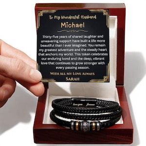 May include: A black braided leather bracelet with silver and gold accents, presented in a wooden gift box. The box includes a card with the text "To My Wonderful Husband Michael" and a loving message.