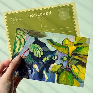 May include: A postcard with a painting of a black cat with green eyes amongst green and yellow plants. The postcard has the word "postcard" printed on it, along with the word "LUCKY". The background is a light green colour.
