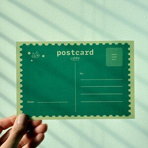 May include: A green postcard with a cat illustration and the word "postcard" in white. The postcard has a stamp-like border and lines for the recipient's address. The text "LUCKY" is below "postcard".