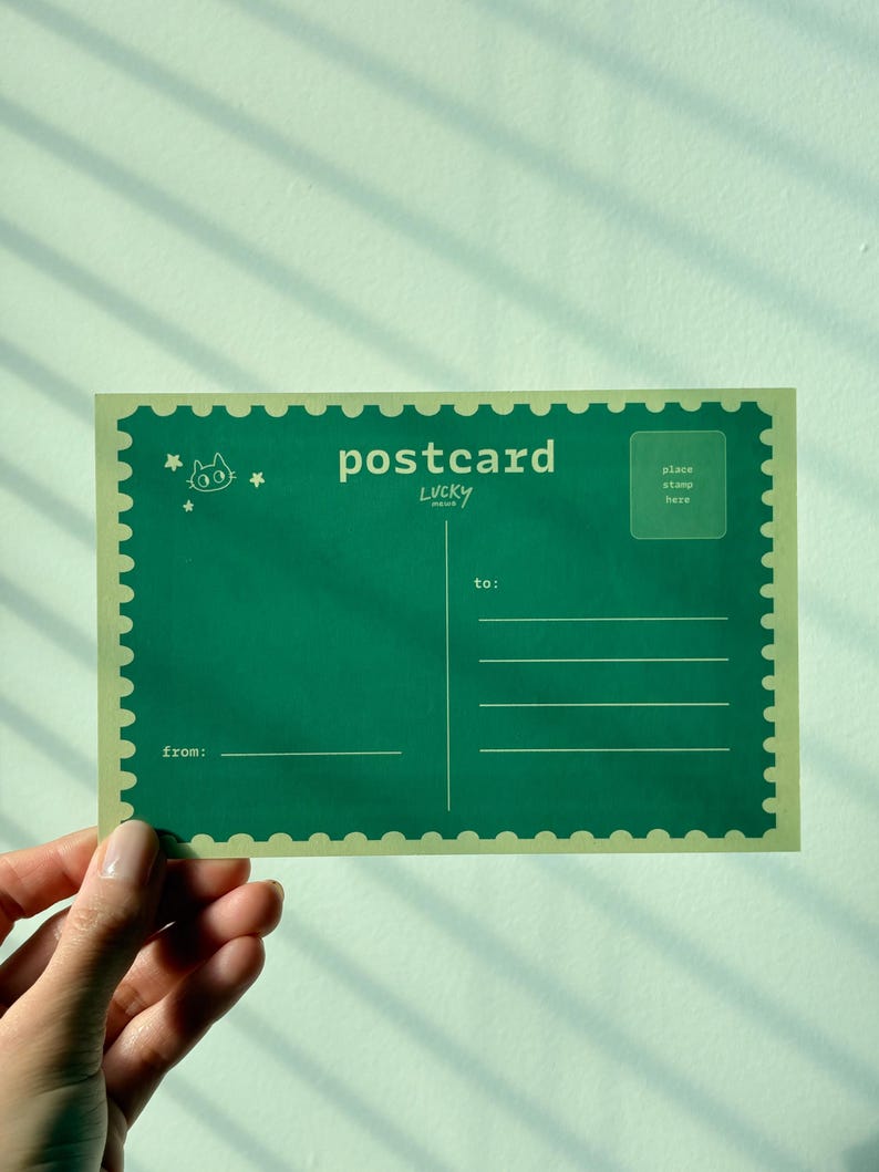 May include: A green postcard with a cat illustration and the word "postcard" in white. The postcard has a stamp-like border and lines for the recipient's address. The text "LUCKY" is below "postcard".