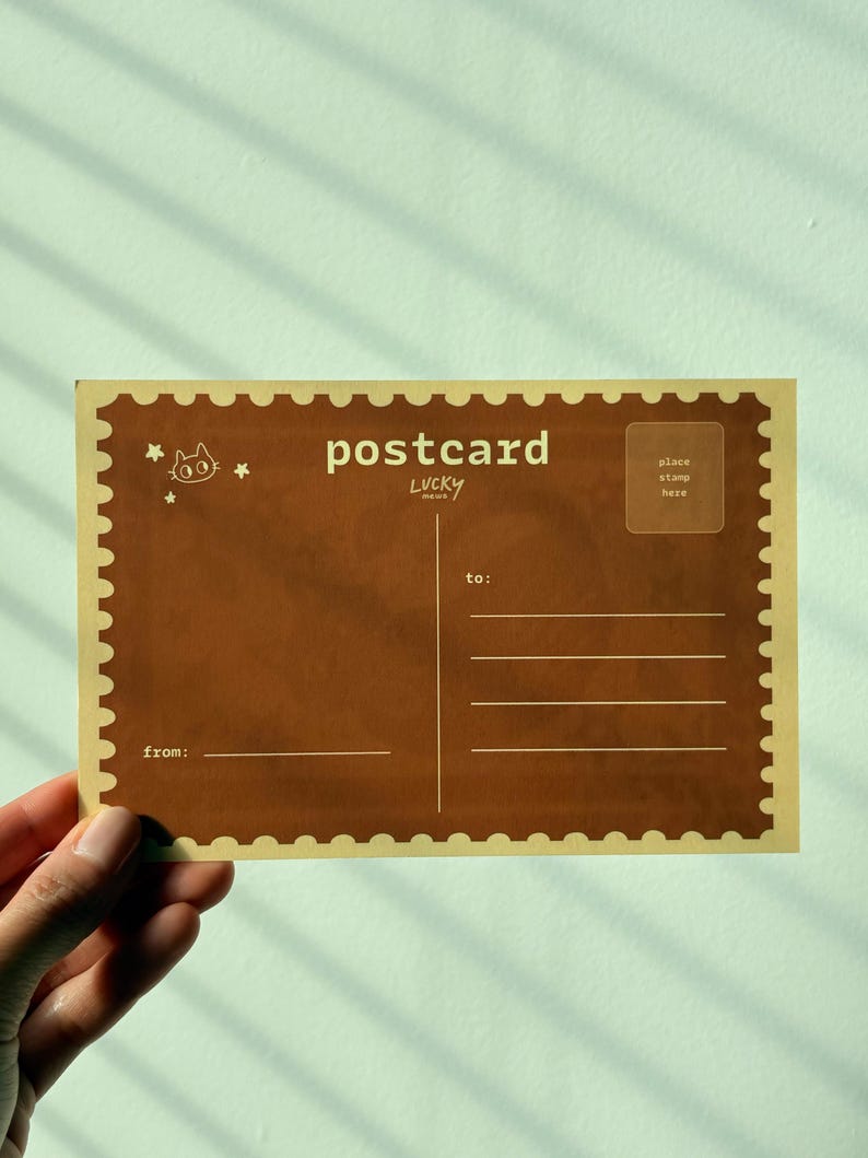 May include: A brown postcard with the word "postcard" in white, along with the word "LUCKY" below it. The postcard has a stamp-like border and includes spaces for "to:" and "from:" and a stamp area.