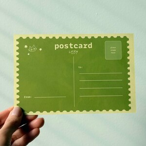May include: A green postcard with a scalloped edge, featuring the word "postcard" and the text "Lucky". The postcard has lines for the recipient's address and a space for a stamp. A small cat illustration is in the upper left corner.