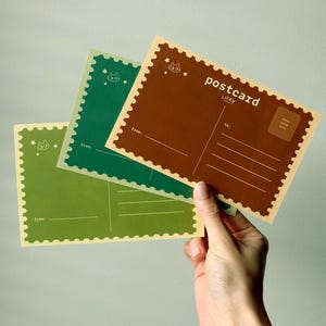 May include: Three postcards in shades of green and brown are held in a hand. The postcards have a scalloped edge and feature a cat illustration and the word "postcard". The back of the postcards have lines for writing and a space for a stamp.