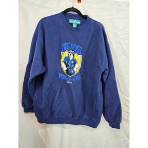 Könnte beinhalten: Ein marineblaues Sweatshirt mit einer Grafik eines Polizeihundes in Uniform, den Worten "BIG DOGS" und "PROTECT & SERVE". Das Sweatshirt hängt an einem schwarzen Kleiderbügel.