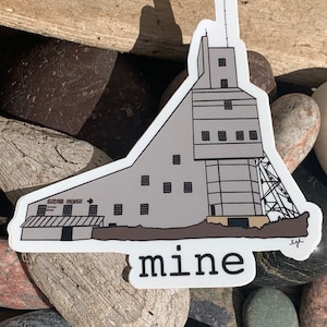May include: A gray and white sticker of a mine building with the text "mine" below it. The building has a sign that says "Gem House".