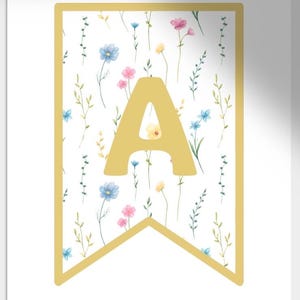 以下が含まれることがあります： 金色の縁取りと大きな金色の文字「A」が付いたバナー。バナーの背景には、白地に青、ピンク、黄色の花と緑の葉が描かれた花柄が施されています。装飾品です。