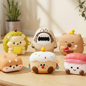 Puede incluir: Una colección de coloridas fundas para AirPods de estilo caricatura con varios diseños. Las fundas incluyen un erizo, una foca, un oso con un pato, un Shiba Inu, una magdalena y un rollo de sushi. Las fundas están hechas de un material liso y brillante.