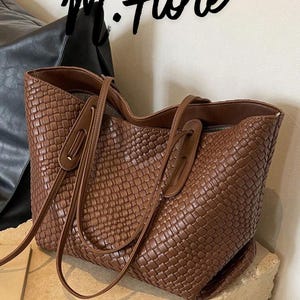 Può includere: Una borsa tote marrone intrecciata con manici lunghi. La borsa ha una forma rettangolare e un design strutturato a trama di vimini. Il testo "M. Fiore" è scritto in corsivo nero in alto.