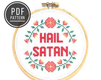 May include: A white embroidery hoop with a cross-stitch design featuring the phrase "Hail Satan" in red lettering surrounded by a wreath of pink flowers and green leaves.