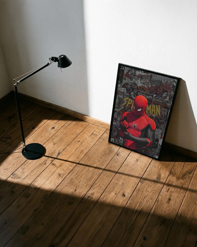 May include: A framed poster featuring Spider-Man in a red and black suit, with the word "Spider-Man" prominently displayed. The background is a collage of comic book panels. A black lamp stands nearby on a wooden floor.