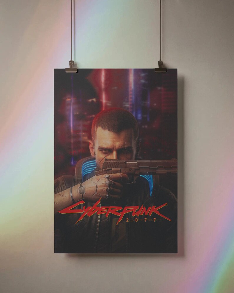 K&ouml;nnte beinhalten: Poster mit einem Mann, der eine Waffe anvisiert, mit dem roten Text "Cyberpunk 2077". Der Hintergrund zeigt eine verschwommene Stadtlandschaft mit roten und blauen Farbt&ouml;nen. Das Poster wird von zwei Clips gehalten.