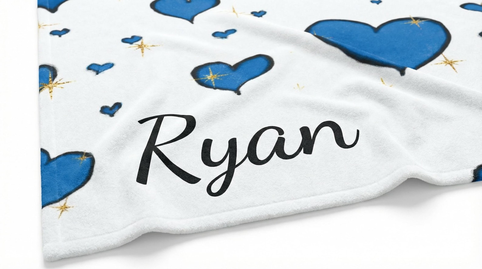 Close-up of the blanket's corner showing blue hearts, gold stars, and the personalized name "Ryan" in script