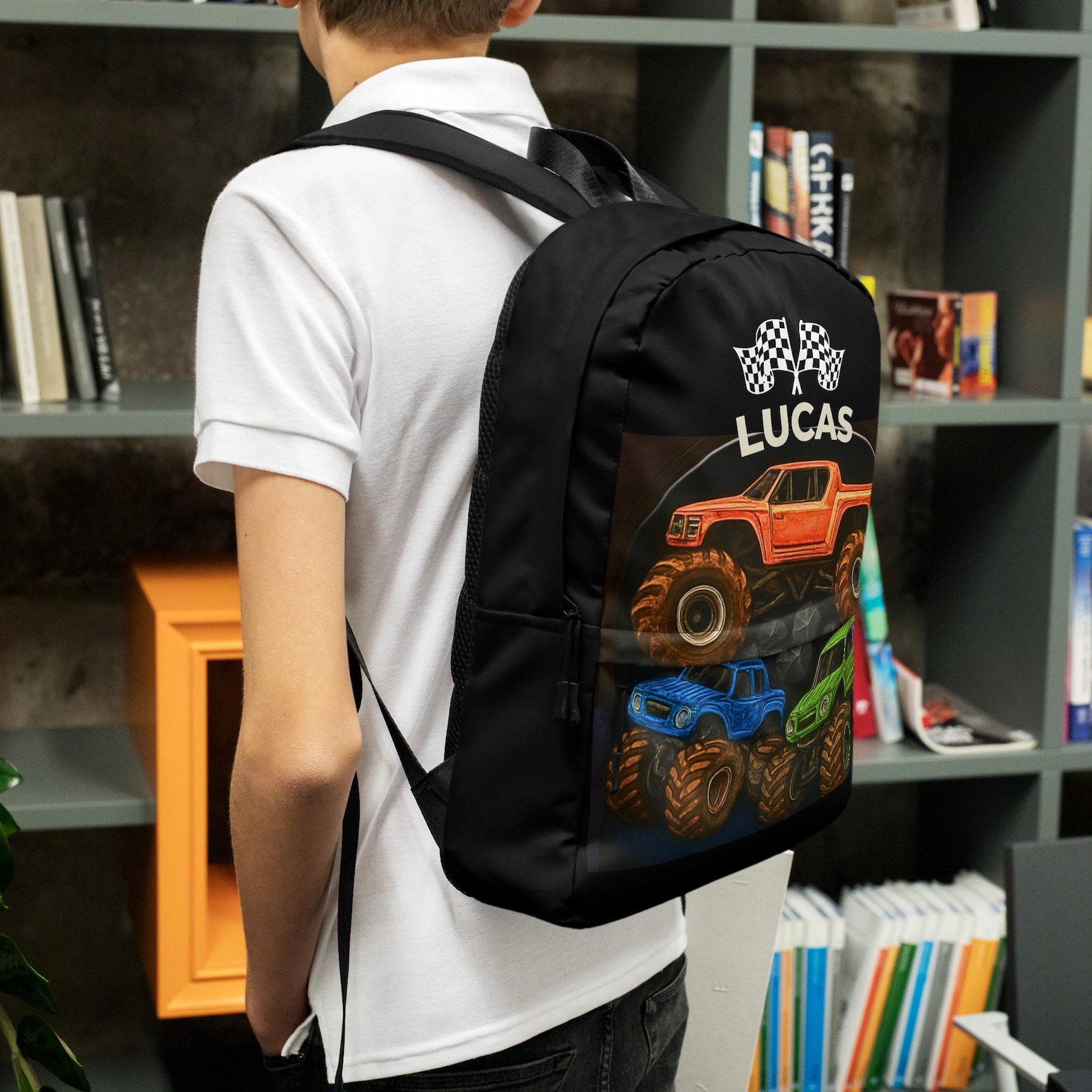 A boy wearing the black monster truck backpack personalized with the name "Lucas", shown from behind near a bookshelf