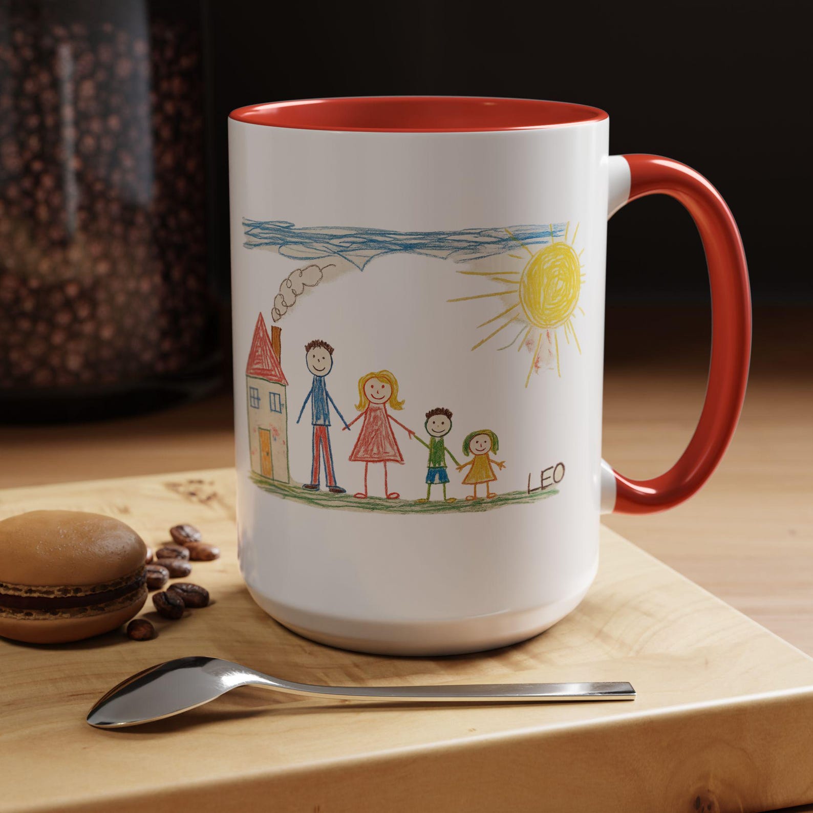 Mug with a red interior and handle, printed with a child's family drawing and the name Leo, on a wooden table with coffee beans and a macaron