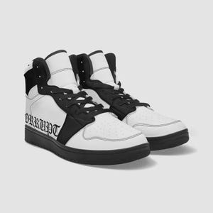 Op de afbeelding: Paar hoge sneakers in wit en zwart. De sneakers hebben een wit bovenwerk met zwarte accenten op de kraag, veters en zool. Het woord "ORRUPT" is in het zwart op de zijkant van de schoen gedrukt.