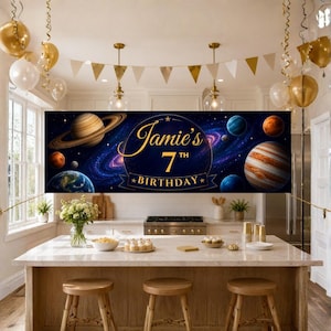 May include: A rectangular horizontal banner featuring a deep blue space theme with planets, stars, and a swirling galaxy. The text "Jamie's 7th BIRTHDAY" is printed in gold script and block lettering in the center of the banner against a dark circle.
