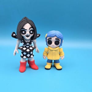 May include: Two stylized figurines. The left figure has black hair, a black and white diamond-patterned dress, and red boots. The right figure has blue hair with a yellow flower, a yellow raincoat, and blue pants with yellow boots. Both have button eyes.