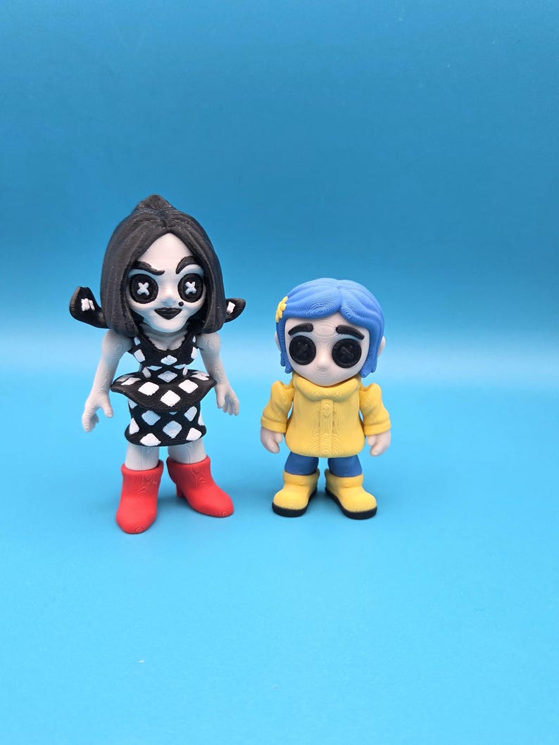 May include: Two stylized figurines. The left figure has black hair, a black and white diamond-patterned dress, and red boots. The right figure has blue hair with a yellow flower, a yellow raincoat, and blue pants with yellow boots. Both have button eyes.
