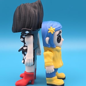 May include: Two stylized figurines standing back-to-back. The left figure has black hair, a black dress with white diamond patterns, and red boots. The right figure has blue hair with a yellow flower accessory, a yellow jacket, and yellow boots.