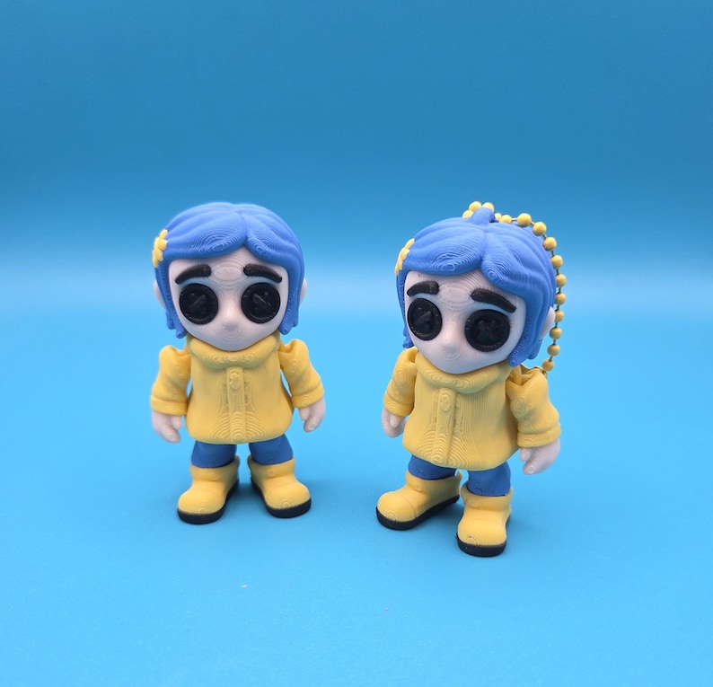 May include: Two small figurines featuring a character with blue hair, black button eyes, a yellow raincoat, and yellow boots. One figurine stands independently, while the other includes a yellow ball chain attached to the top of its head.