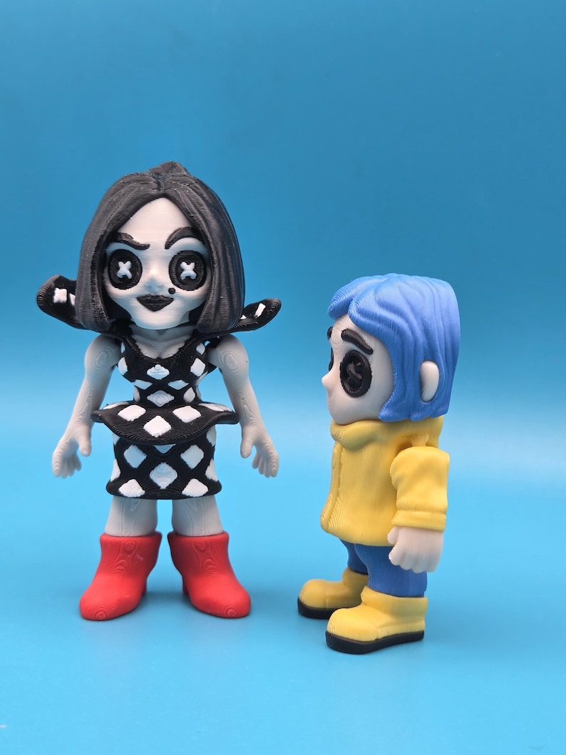 May include: Two stylized figurines. The left figure has black hair, button eyes, and a black and white diamond-patterned dress with red boots. The right figure has blue hair, button eyes, a yellow hooded jacket, blue pants, and yellow boots.