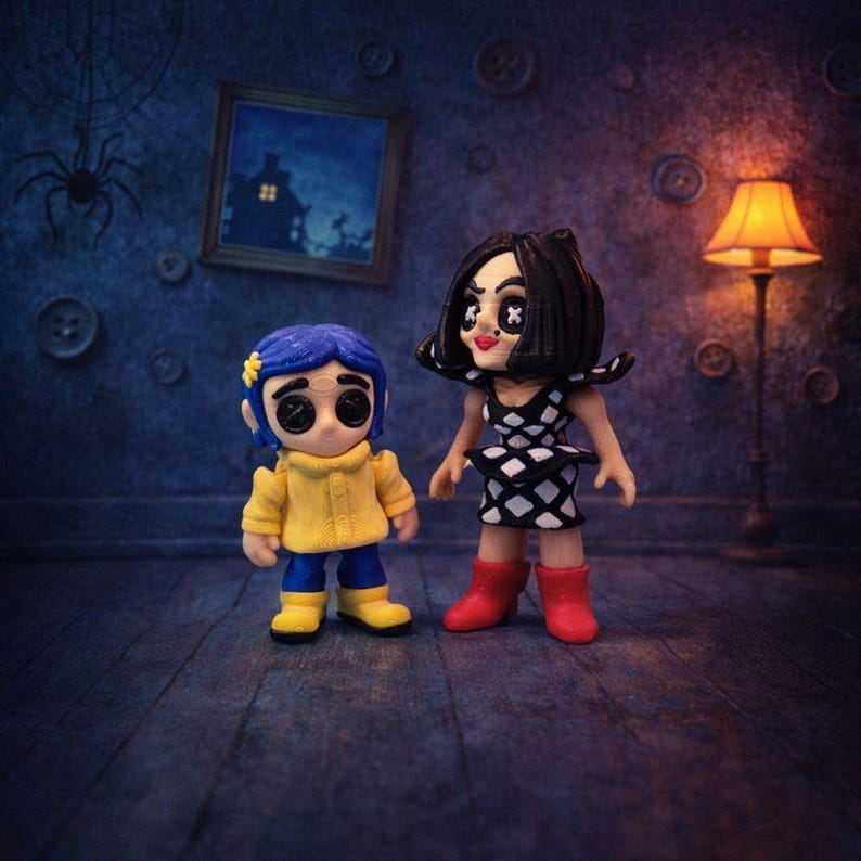May include: Two small figurines standing side by side. The left figure has blue hair, a yellow raincoat, and black button eyes. The right figure has black hair, a black and white diamond-patterned dress, red boots, and black button eyes.