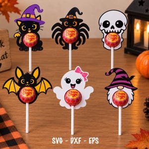 May include: Six Halloween-themed lollipop holders featuring a black cat in a purple hat, a spider in a black hat, a white skull, a black bat, a white ghost with a pink bow, and a gnome in a purple striped hat, each holding a Chupa Chups lollipop.
