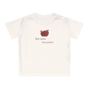 Peut inclure: T-shirt de bébé blanc cassé à manches courtes et fermetures à boutons-pression au niveau de l'épaule. Le t-shirt présente un motif de pomme marron et le texte français "Haut comme trois pommes."