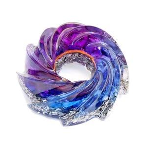 Può includere: Una scultura astratta decorativa con un design a spirale circolare. La scultura presenta una sfumatura di colori, che passa dal viola intenso al blu vibrante. Il centro ha un filo color rame e la base ha accenti color argento.