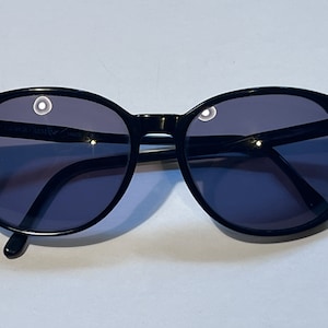 May include: Black round sunglasses with dark lenses. The sunglasses have a thin black frame.