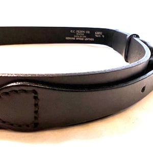 K&ouml;nnte beinhalten: Nahaufnahme eines schwarzen Lederg&uuml;rtels mit silberner Schnalle. Der G&uuml;rtel hat eine gen&auml;hte Lederschlaufe und ist mit "Genuine Bridle Leather" und "Made in USA" gekennzeichnet. Der G&uuml;rtel ist etwa 3,18 cm breit.