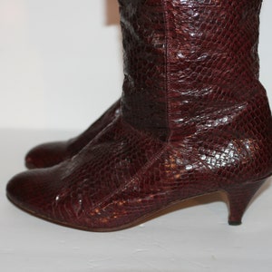 May include: A pair of burgundy leather heeled boots with a snakeskin pattern.