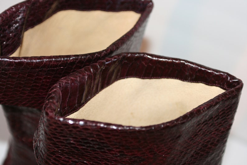 May include: Close-up of the inside of a pair of burgundy leather boots. The boots have a snakeskin pattern and a soft beige lining.