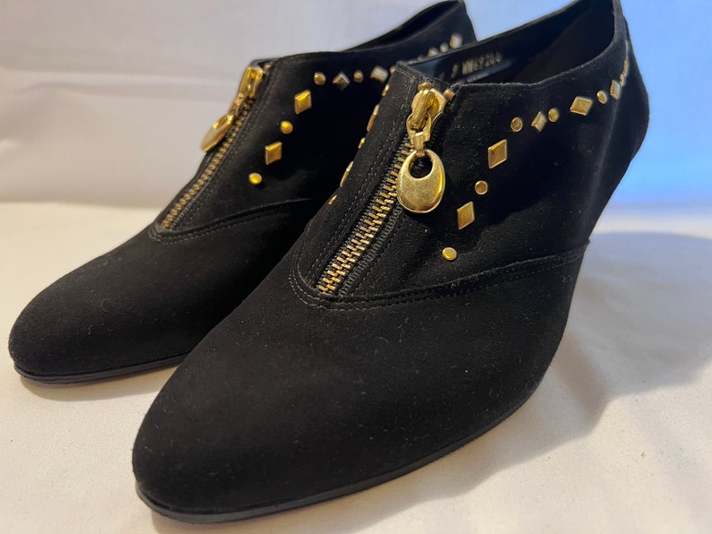 May include: A pair of black suede ankle boots with gold zipper accents and gold studs. The boots have a pointed toe and a low heel.