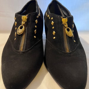 May include: A pair of black suede ankle boots with gold-tone zippers and studs. The boots have a pointed toe and a low heel.